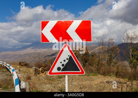 Ein Straßenschild warnt die Fahrer vor einer bevorstehenden scharfen Linkskurve und überblickt eine malerische Landschaft mit Bergen und Wolken. Stockfoto