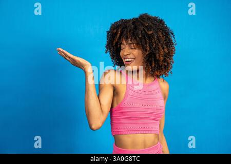 Lächelnde Frau, die etwas auf der Handfläche mit blauem Hintergrund zeigt Stockfoto