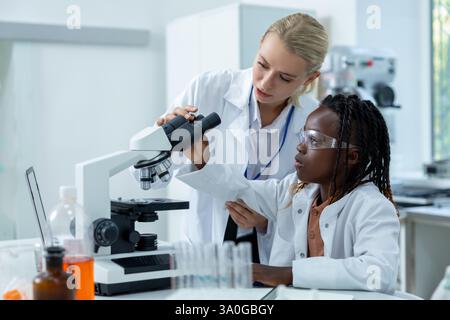 Blonder Lehrer im Weißen Labor, der einem Schüler erklärt, wie man mit dem Mikroskop arbeitet Stockfoto