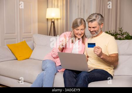 Ein reifes Paar sitzt zusammen auf einem Sofa und bezahlt online Stockfoto