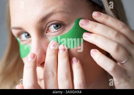Nahaufnahme einer kaukasischen Millennial-Frau ohne Make-up, die grünes Gel feuchtigkeitsspendende Flecken unter ihren Augen aufträgt Stockfoto