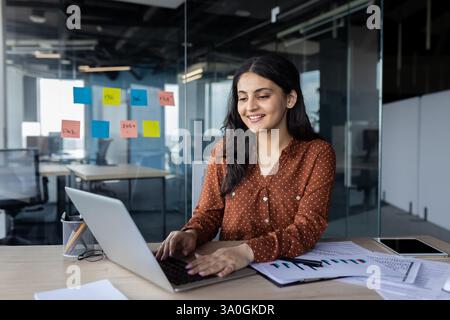 Glückliche Frau, die am Arbeitsplatz im Büro mit einem Laptop arbeitet. Firmenmitarbeiter, der über die Tastatur eingegeben wird. Erfolgreiche Geschäftsfrau in lässiger Kleidung, Investor. Stockfoto