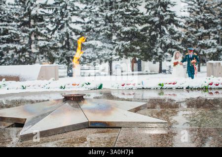 Ewige Flamme brennt auf einem Denkmal in einer verschneiten Umgebung mit einem verschwommenen Paar im Hintergrund Stockfoto