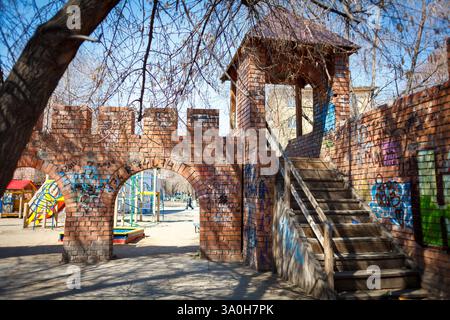 Ein gemauerter Torbogen in einem Spielplatz mit Treppen nach oben, umgeben von Schaukeln und Wohngebäuden im Hintergrund Stockfoto