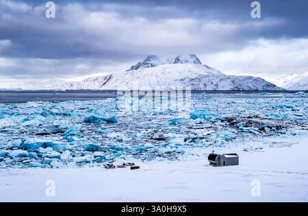 Eine ruhige Winterlandschaft mit einem gefrorenen Meer mit großen Eisbergen und einem schneebedeckten Berg im Hintergrund. Der Himmel ist bewölkt mit dramatischen Stockfoto