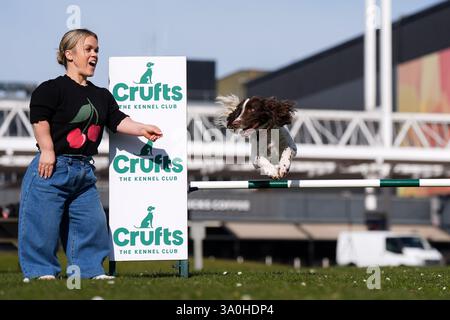 Die Paralympierin Ellie Simmonds, die in der Present-Line-up für die Crufts TV-Show neu angekündigt wurde, jubelt dem englischen Springer Spaniel Ozzy, der während der offiziellen Veröffentlichung der Crufts Dog Show 2025 im NEC Birmingham über ein Hindernis springt. Bilddatum: Dienstag, 4. März 2025. Stockfoto
