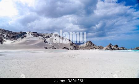 Ein atemberaubender Blick auf die einzigartige Landschaft von Socotra mit weißem Sand, felsigen Felsvorsprüngen und einem weitläufigen Himmel mit Wolken. Stockfoto