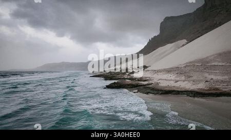 Die Wellen brechen unter den dunklen Wolken in Socotra gegen die Küste und zeigen einzigartige Geologie und wilde Natur. Stockfoto