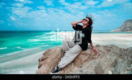 Ein Reisender entspannt sich auf einer felsigen Oberfläche und genießt die Sonne und den atemberaubenden Blick auf das Meer im wunderschönen Socotra-Archipel. Stockfoto