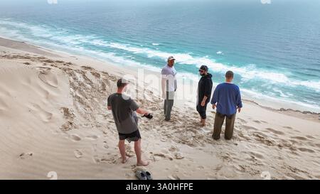 Vier Touristen genießen die atemberaubende Sandlandschaft von Socotra und genießen die wunderschöne Küste und die Meereswellen. Stockfoto