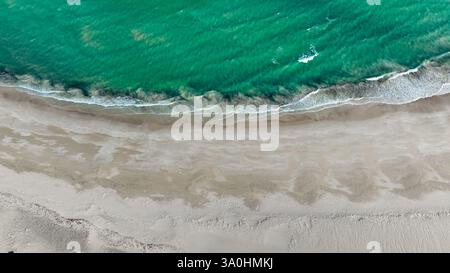 Die Wellen schlängeln sanft am Sandstrand der Insel Socotra und enthüllen das lebhafte türkisfarbene Wasser unter dem klaren Himmel. Stockfoto
