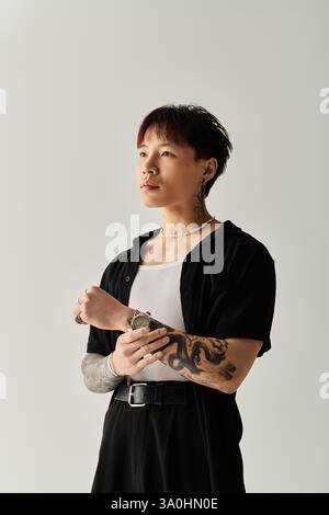 Selbstbewusster junger Mann zeigt seinen stilvollen Look mit Tattoos in einem modernen, minimalistischen Raum. Stockfoto