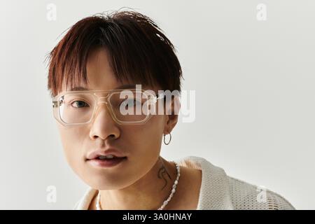 Selbstbewusster junger Mann zeigt mit Brillen in einer minimalistischen Studioumgebung Modebewusstsein. Stockfoto