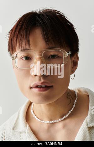 Der junge Mann präsentiert seinen trendigen Stil mit Brillen und einzigartigem Schmuck in einem modernen Ambiente. Stockfoto