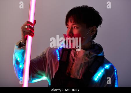 Junger und gutaussehender asiatischer Mann zeigt einen modernen Stil mit Neonelementen in der Dämmerung. Stockfoto