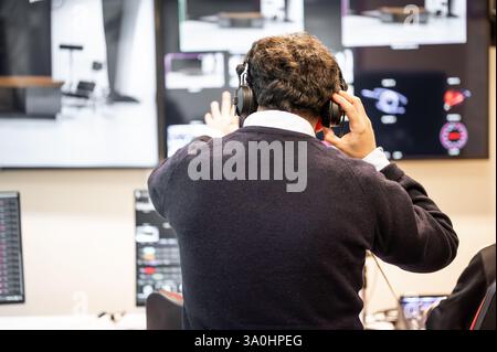 Ein Fernsehregisseur in einem Senderaum, der aktiv eine Live-Produktion leitet. Umgeben von mehreren Bildschirmen trägt der Regisseur ein Headset und bewegt sich in Richtung eines Video-Umschalters. Stockfoto