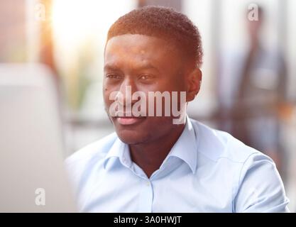 Nachdenklicher, ernster afrikaner sitzt mit Laptop und denkt an das Projekt Stockfoto
