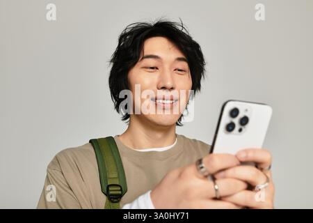 Ein hübscher junger asiatischer Mann lächelt hell, während er sein Smartphone in einer stilvollen Umgebung bedient. Stockfoto