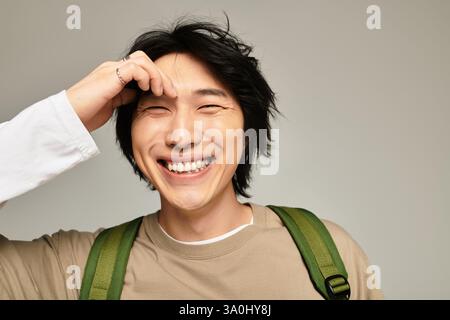 Ein junger und gutaussehender asiatischer Mann lächelt hell, während er spielerisch eine Hand durch sein Haar fährt. Stockfoto