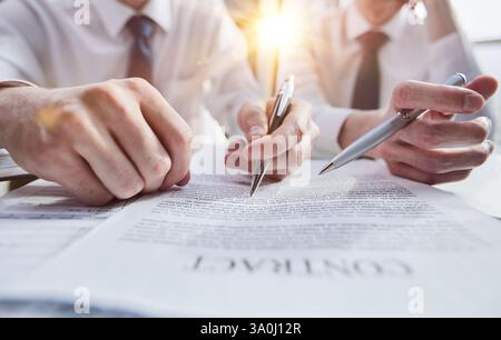 Nahaufnahme von Geschäftsleuten, die einen Nahaufnahmevertrag prüfen, während sie an einem Tisch sitzen Stockfoto