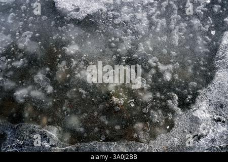 Die Natureisoberfläche mit gefrorenen Luftblasen, Nahaufnahme. Abstrakter Winterhintergrund. Makroluft und Wassertropfen auf Glas Stockfoto