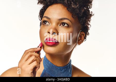 Eine schöne afroamerikanische Frau trägt anmutig roten Lippenstift auf, während sie elegant posiert. Stockfoto