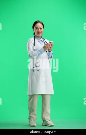 Eine Ärztin in voller Länge, auf grünem Hintergrund, telefoniert Stockfoto