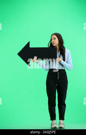 Eine Frau in voller Länge auf grünem Hintergrund zeigt einen Pfeil zur Seite Stockfoto
