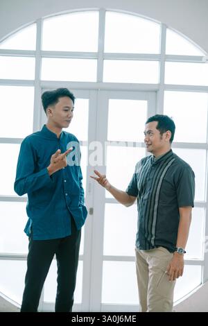 Zwei asiatische Männer spielen ein freundliches Spiel aus Stein, Papier, Schere. Sie stehen drinnen und kommunizieren mit Gesten und Ausdrücken in einem leichten Ro Stockfoto