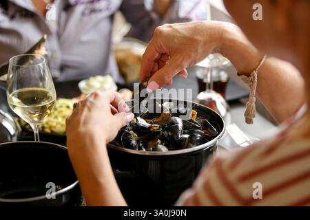 Frauenhände halten Muscheln über einer Muschelpfanne in einem Fischrestaurant mit einem Glas Weißwein Stockfoto