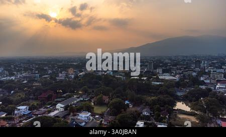 Aus der Vogelperspektive von Chiang Mai, Thailand, mit urbaner Zersiedelung, üppigem Grün und der Silhouette des Doi Suthep Berges vor der untergehenden Sonne mit verschmutzten Stockfoto