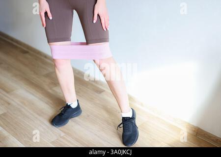 Frau, die zu Hause Hocktraining mit Widerstandsband macht, Sportbekleidung trägt und sich auf Fitness konzentriert Stockfoto