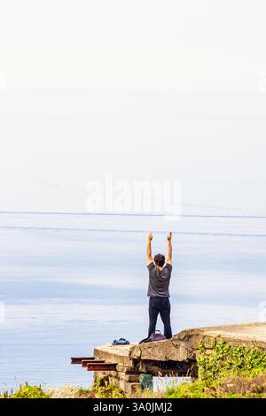 Allein ein Mann, der Yoga praktiziert und seine Arme am Meer ausstreckt Stockfoto