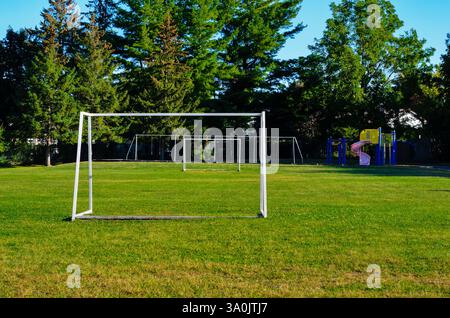Empty soccer playing field at a schoolyard, with white goals in the morning sun and trees in the background Stockfoto