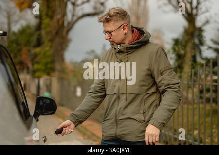 Junger attraktiver Mann steht auf der Straße mit Einem Auto und öffnet die Autotür mit Einem Schlüssel Stockfoto
