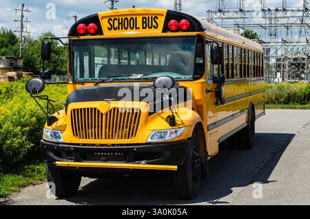 Vorderansicht eines gelben Schulbusses, der vor einer Unterstation unter dunklem Himmel geparkt ist Stockfoto
