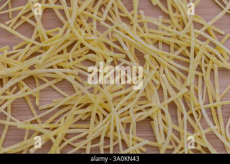 Eine Nahaufnahme von gelben Spaghetti-Nudeln auf einem Tisch, ein Stapel dünner und langer Nudelstreifen, die in einer einzigen Zeile auf einem Holzhintergrund liegen. Stockfoto