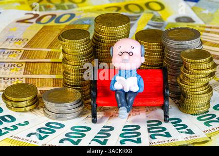 Symbol des finanziell gesicherten Alters, eine Puppenfigur eines alten Mannes, die auf einer Bank sitzt und ein Buch liest Stockfoto