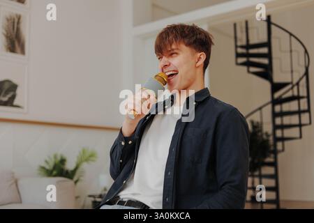 Der junge 20-Jährige trägt zu Hause ein blaues Hemd und singt im Karaoke-Mikrofon Stockfoto