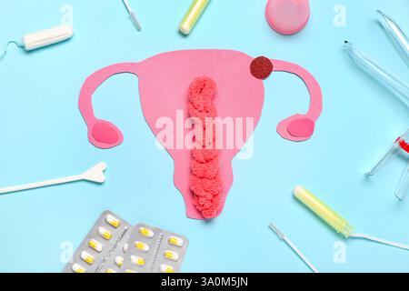 Papieruterus mit gynäkologischem Spekulum, Pillen und Tampons auf blauem Hintergrund Stockfoto