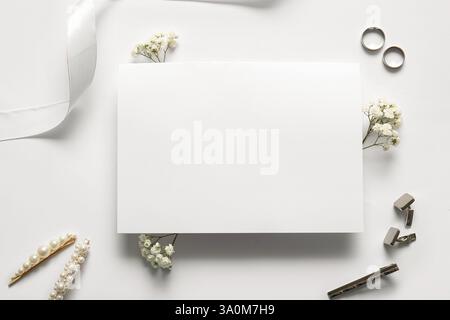 Leere Einladungskarte, Eheringe und Blumen auf weißem Hintergrund Stockfoto