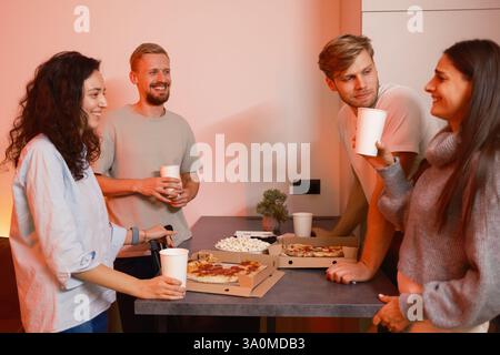 Eine Gruppe von Freunden genießt gemeinsam Pizza und Getränke bei einem gemütlichen Treffen zu Hause Stockfoto