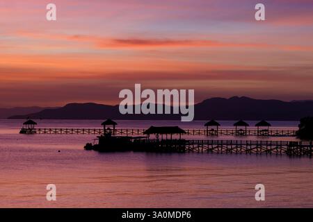 Blick auf den Sonnenaufgang auf die Docks und Tiki-Hütten auf der Insel Seraja Kecil, auch bekannt als Seraya, vor der Küste von Labuan Bajo, Komodo-Inseln, Indonesien. Stockfoto