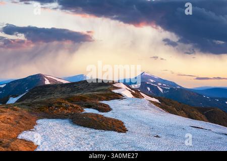 Frühlingsregen in den hohen Bergen. Schneebedeckte Hügel und hohe Gipfel, die von der untergehenden Sonne erstrahlen. Landschaftsfotografie Stockfoto