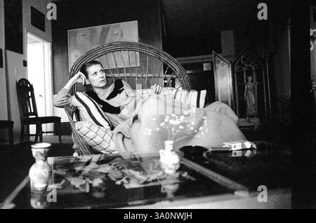 Los Angeles, CA, USA, ca. 1985. Frau in elegantem Wohnzimmer, die sich auf einem großen Stuhl entspannt und eine Zigarette raucht. Stockfoto