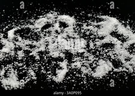 Weiße Tafelsalzkristalle sind auf schwarzem Hintergrund verstreut. Stockfoto