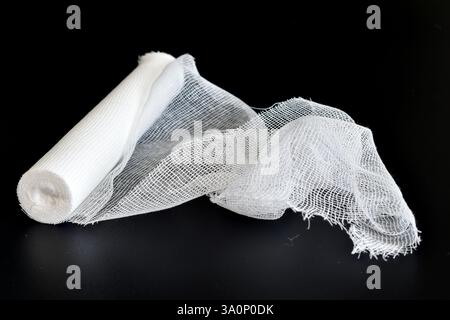 Eine Rolle Mullverband liegt auf schwarzem Hintergrund. Stockfoto