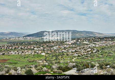Aus nächster Nähe sehen Sie eine malerische Stadt mit roten Dächern, eingebettet in ein üppiges Tal, umgeben von sanften Hügeln und Bergen Stockfoto