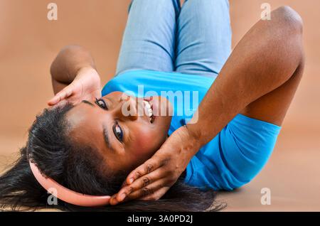 Glückliche junge Frau, die auf dem Boden liegt und Musik mit Kopfhörern genießt Stockfoto