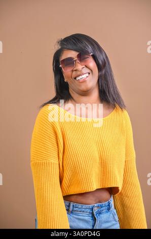 Studio-Porträt einer fröhlichen afroamerikanerin, die einen gelben Pullover und eine Sonnenbrille trägt und breit lächelt Stockfoto